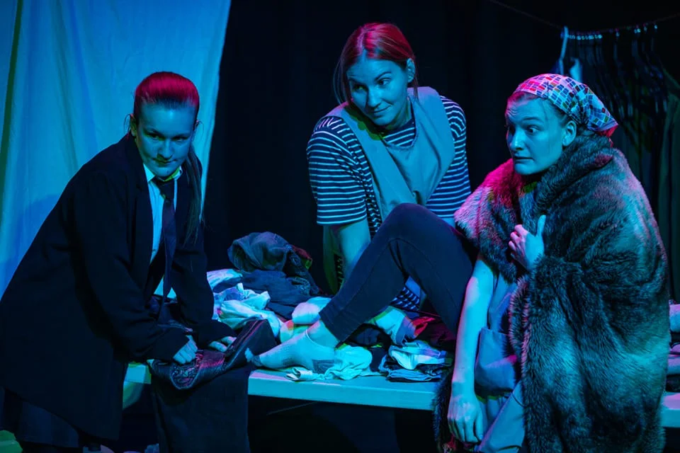Three performers sharing a scene under blue and magenta stage lighting