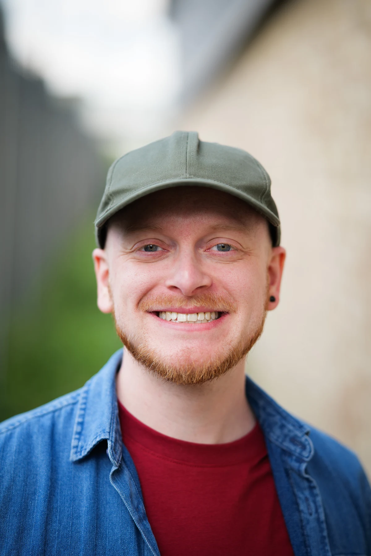Richard Bland smiling, wearing a green cap, denim shirt and burgundy T-shirt